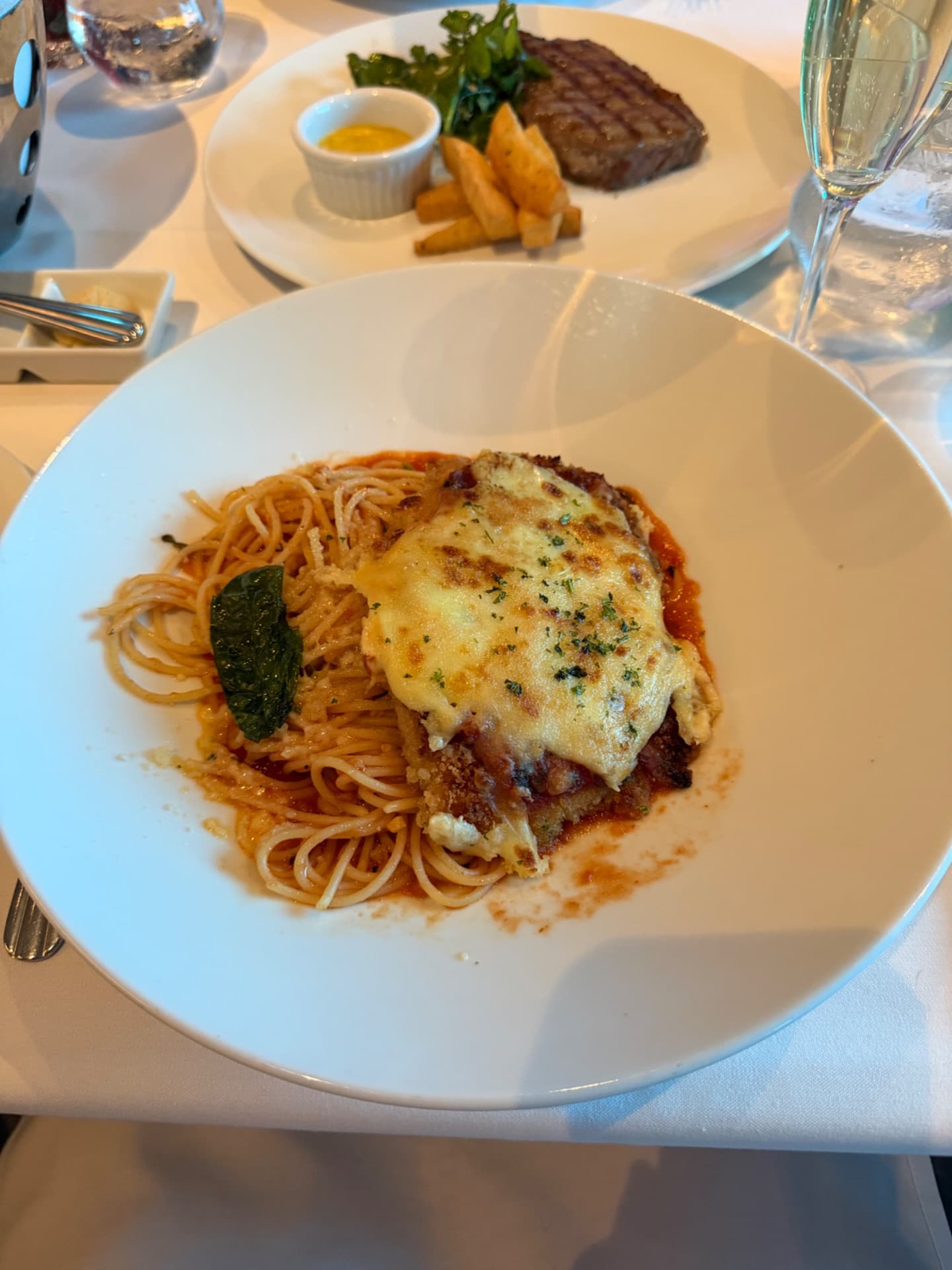 Elegant plated spaghetti bolognese with melted cheese topped on a white plate, served at a fine dining restaurant on a cruise ship.