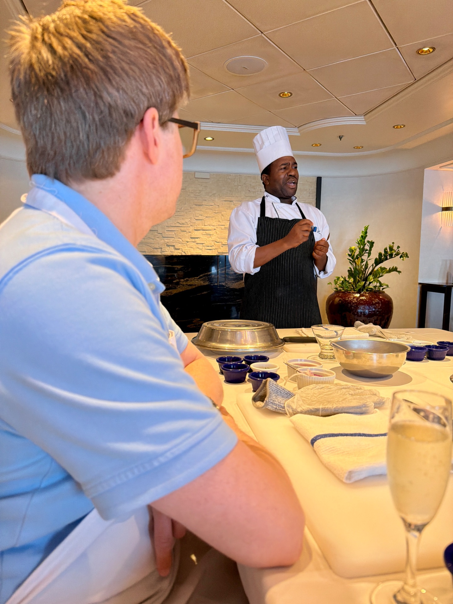 Chef demonstrating cooking techniques to a guest during a culinary class on a cruise ship.
