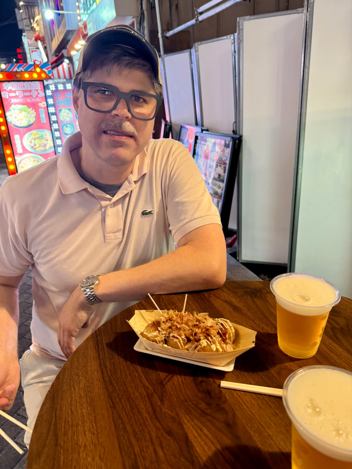 Man enjoying Asian cuisine and beer at a casual dining venue on a cruise ship, with neon signs visible in the background.