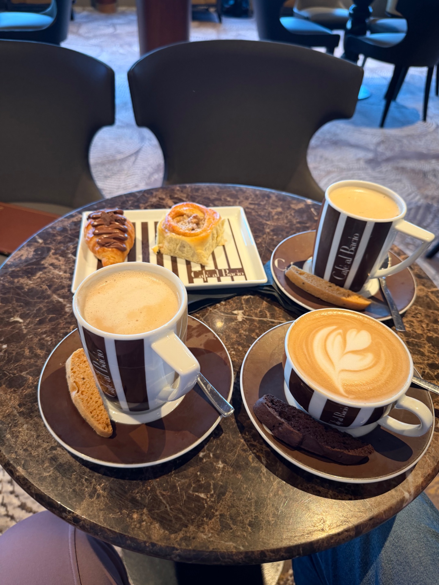 Coffee and pastries served on a round table at a cruise ship café with latte art and biscotti.