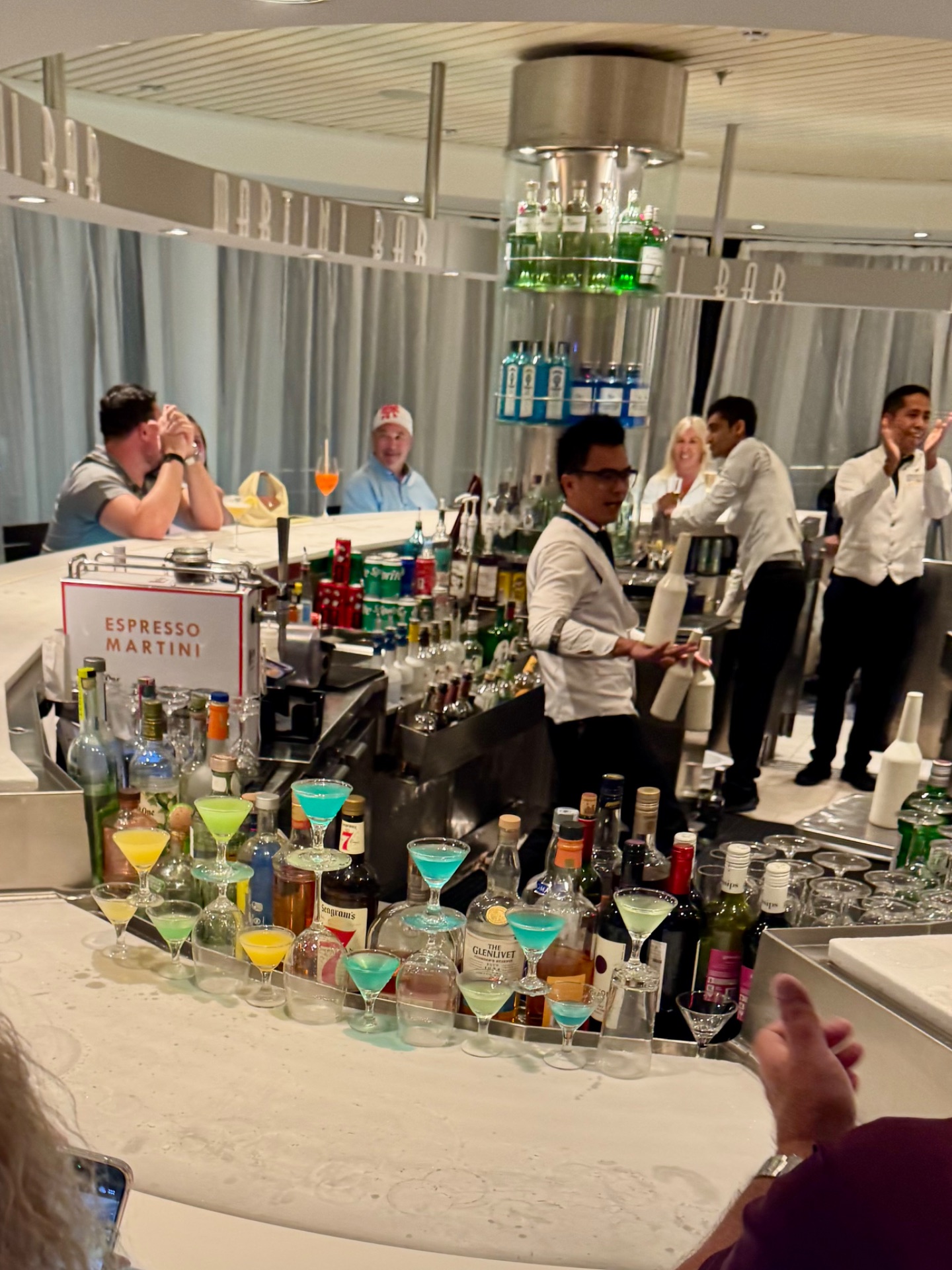 Bartenders demonstrate cocktail mixing at an Espresso Martini bar during a cruise ship event with attendees watching.