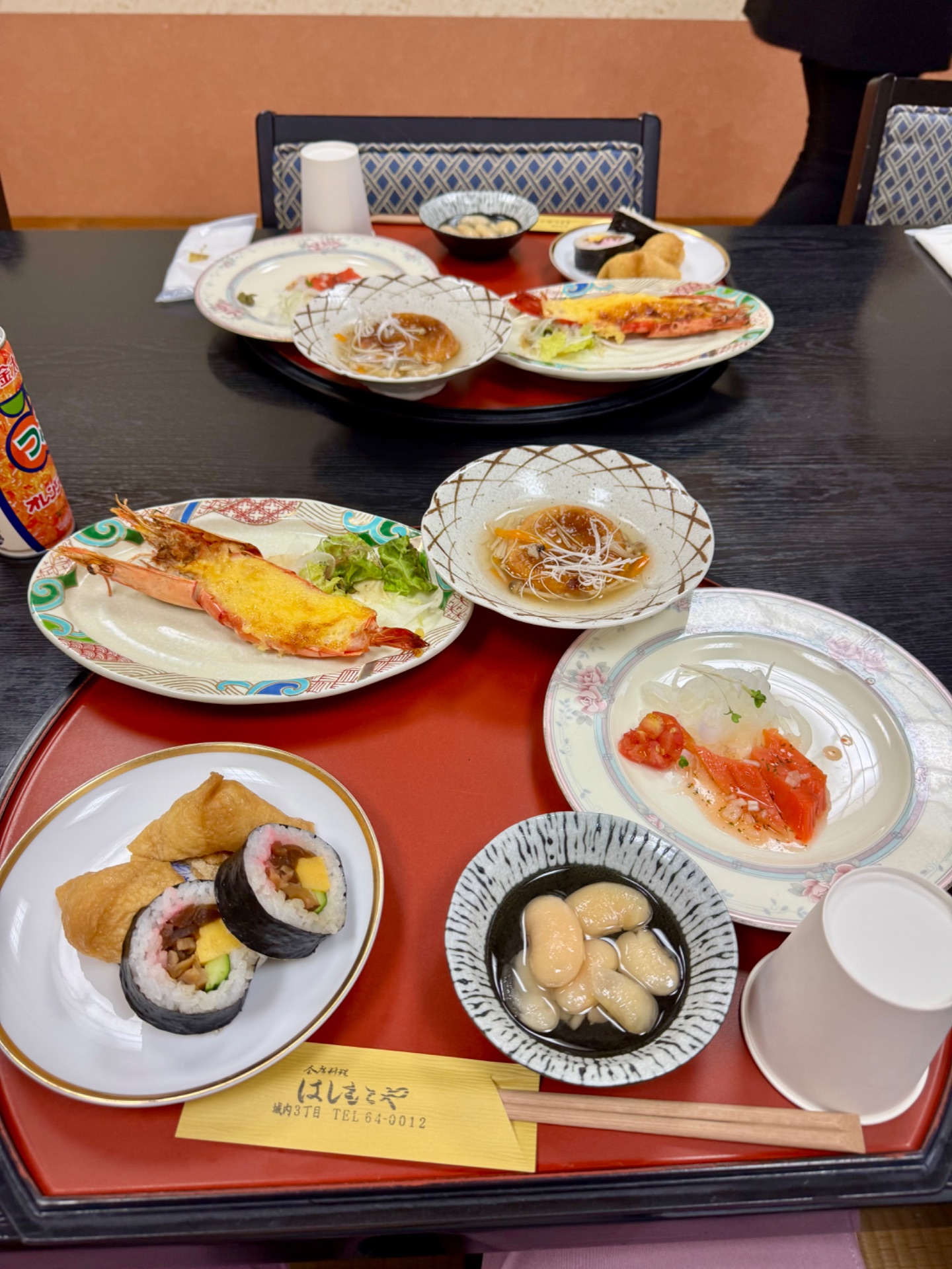 Japanese dining experience with multiple dishes including grilled shrimp, sushi rolls, noodles, and seafood on red trays.