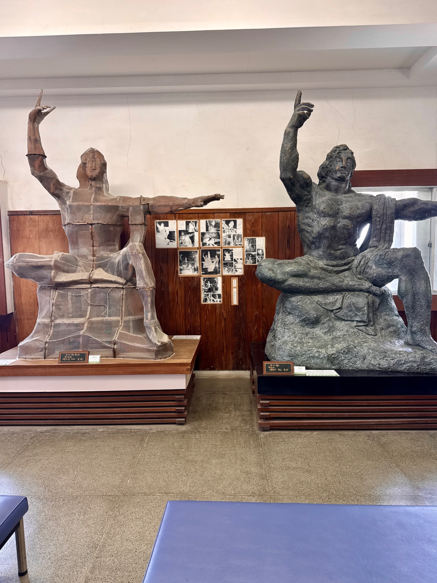 Two large sculptural monuments depicting figures with raised arms displayed in an indoor museum gallery space with wooden panels.