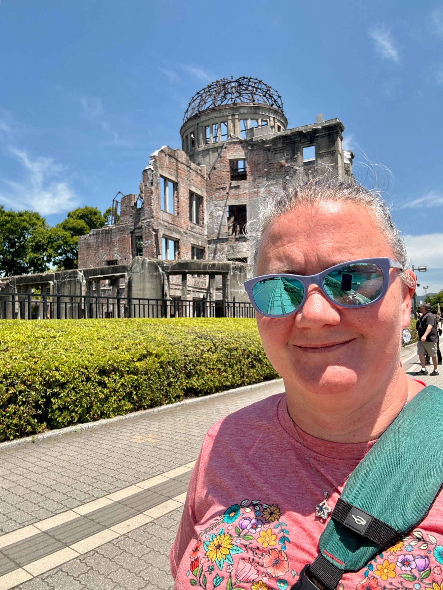 Tourist posing at Hiroshima Peace Memorial Park with the A-Bomb Dome ruins in background under blue sky