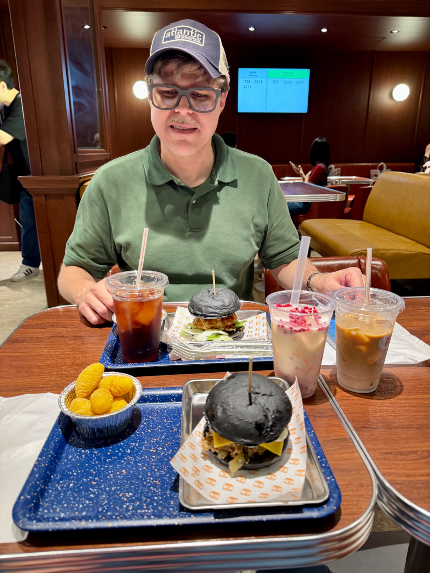 Person enjoying black burgers and drinks at a cruise ship dining venue with ocean view windows.