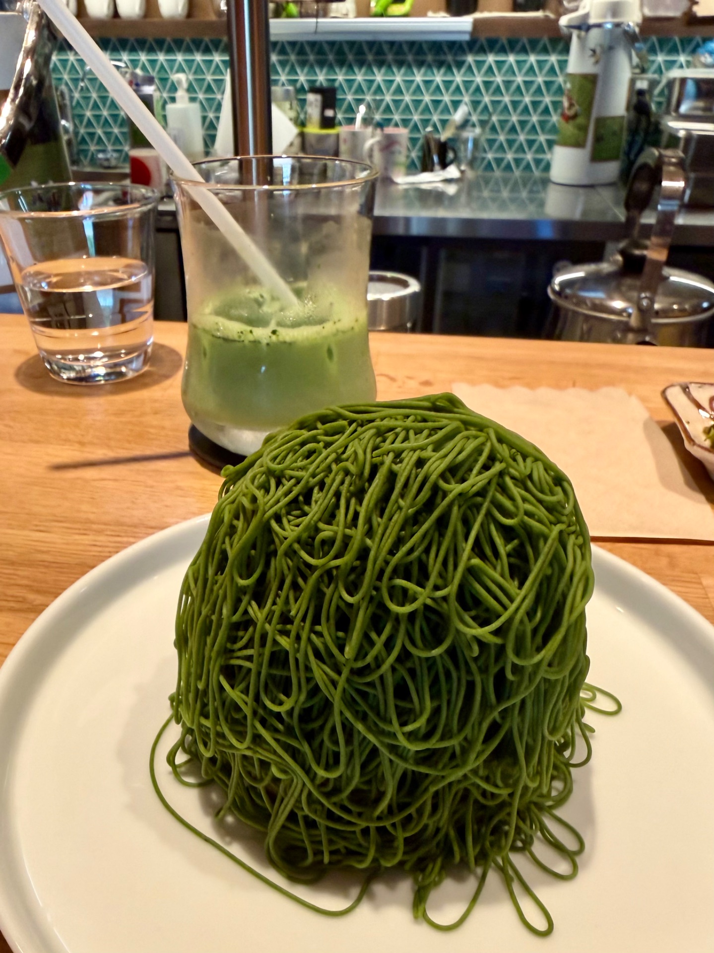 Green spinach noodles on white plate with matcha drink at restaurant counter.