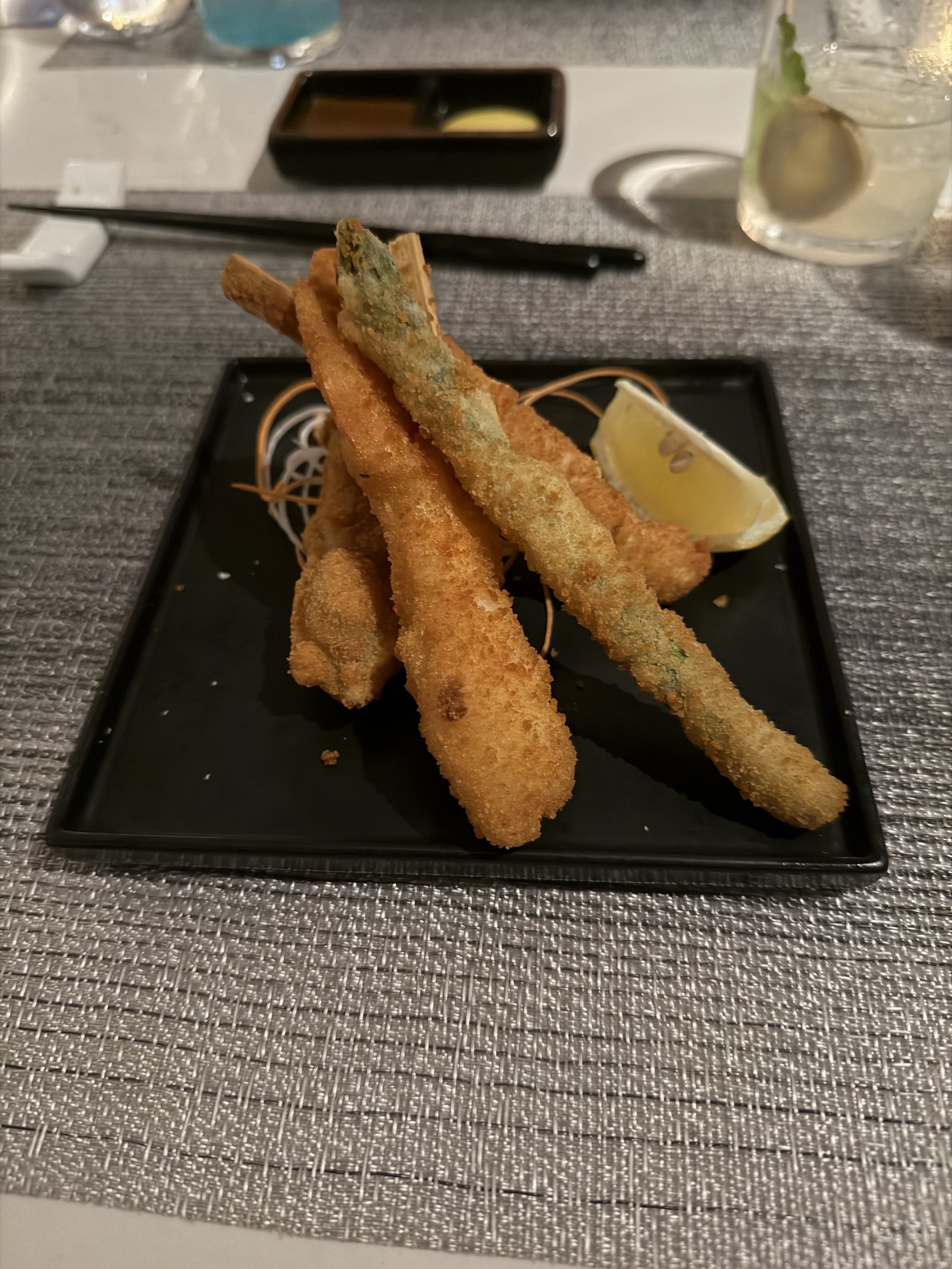 Crispy tempura shrimp with lemon wedge on black plate