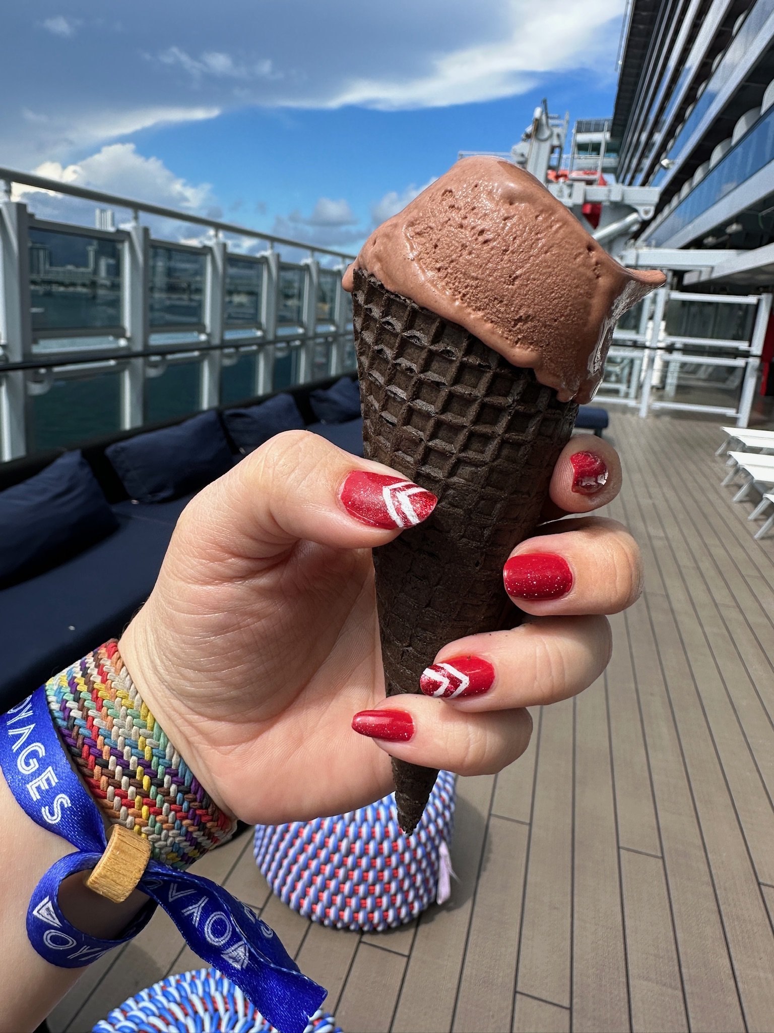 Chocolate ice cream cone on cruise ship deck with red nail polish
