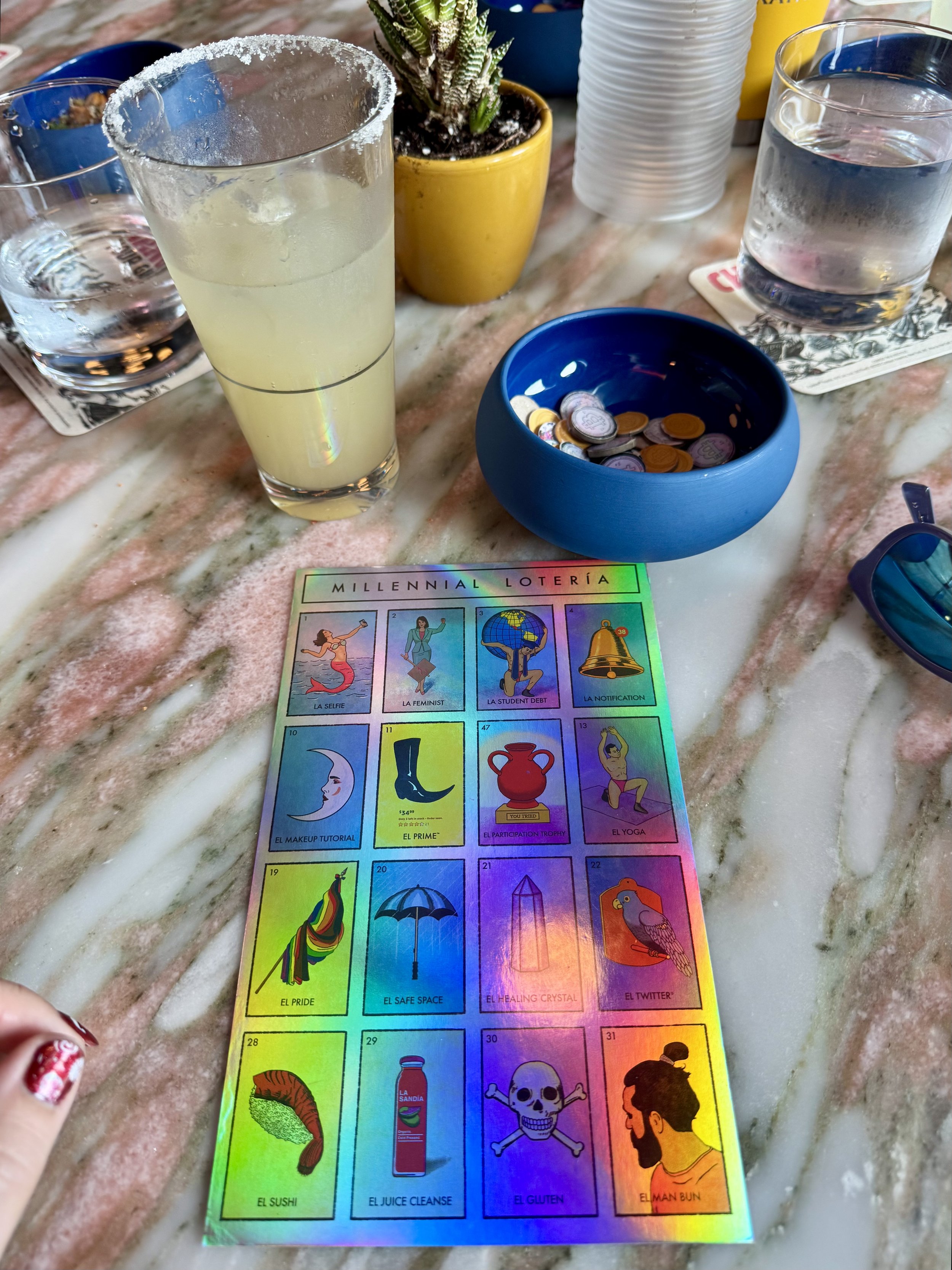 Millennial Loteria game with margarita and coins on marble table