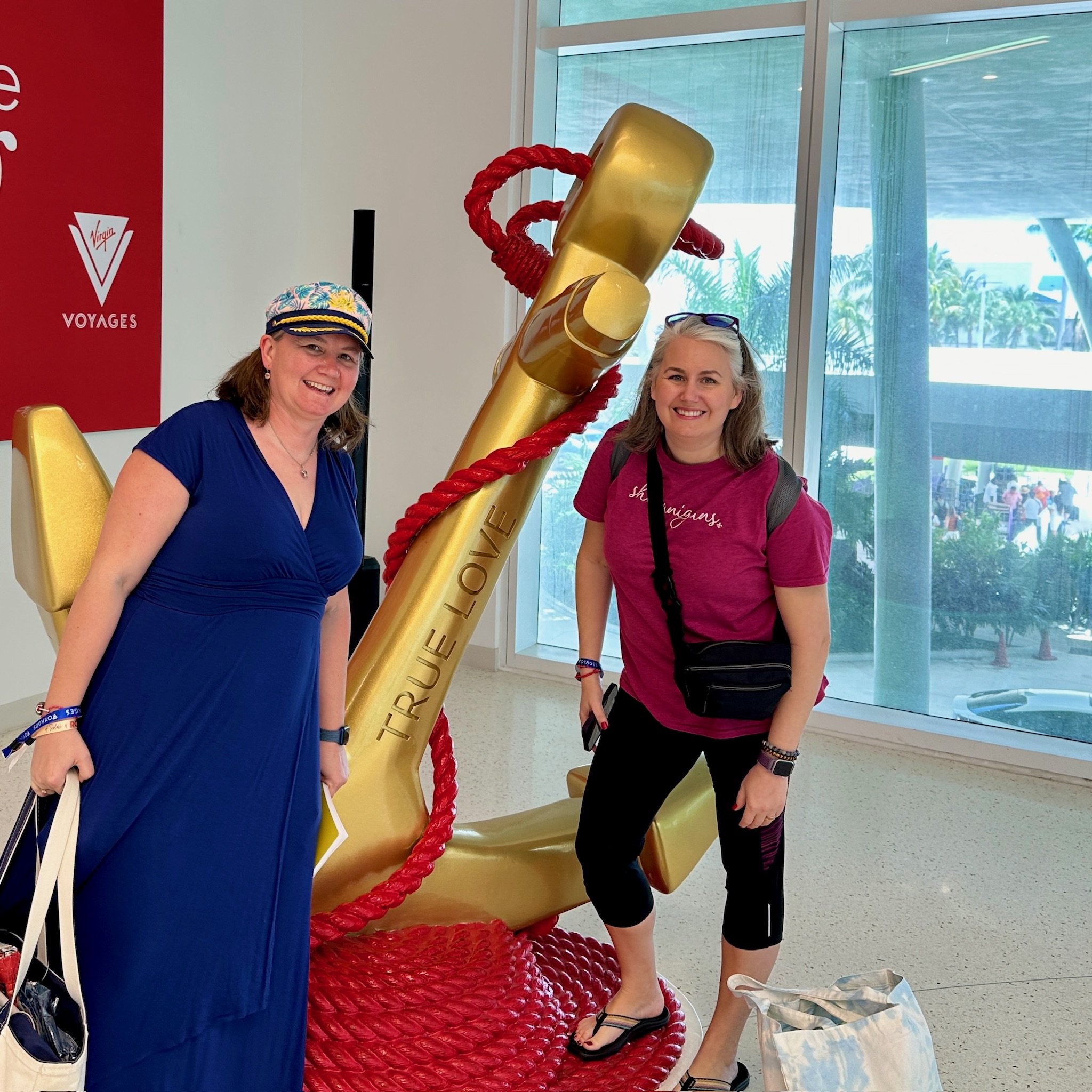 Two women posing with giant golden cruise ship anchor statue