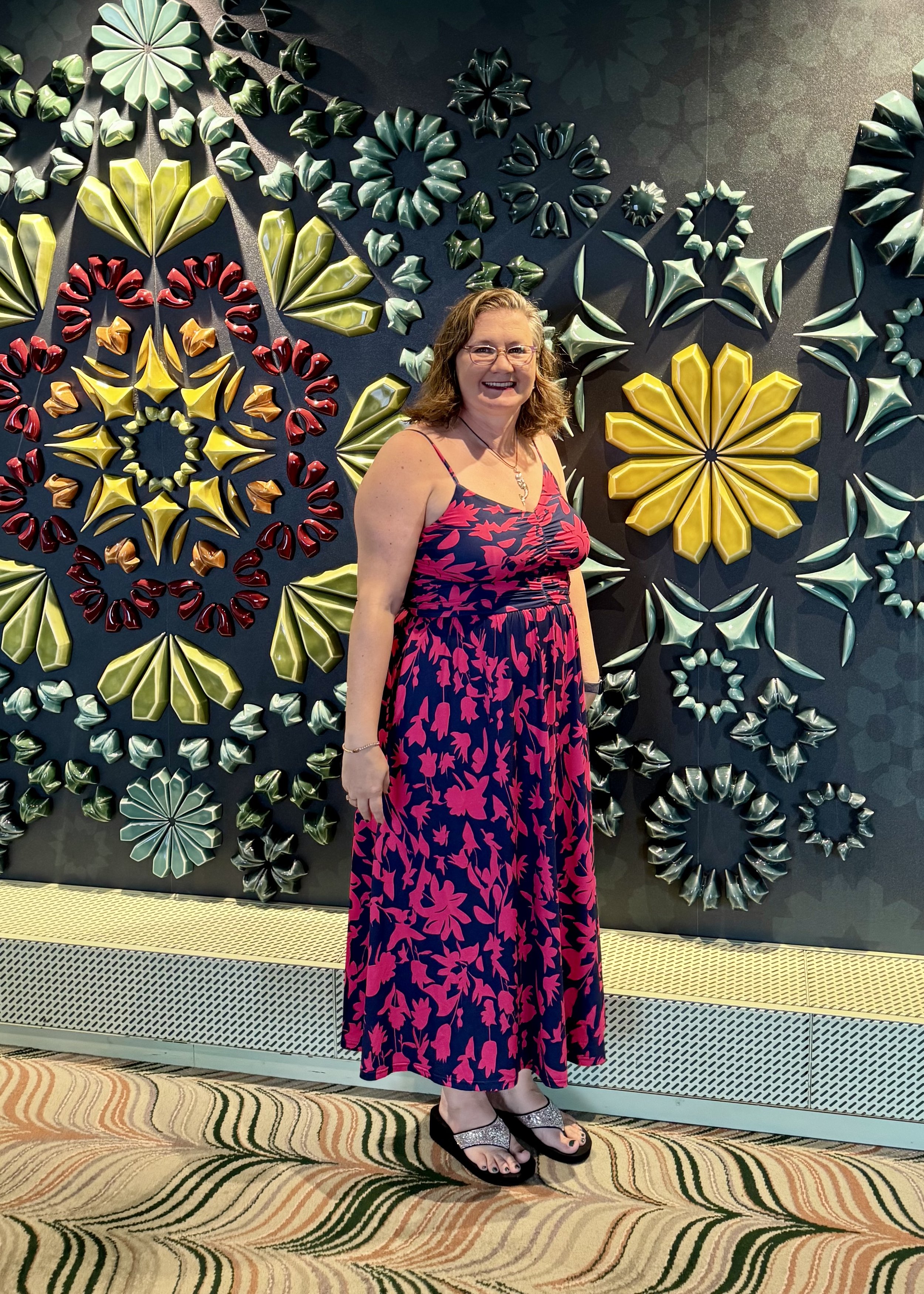 Woman poses before colorful floral wall art installation