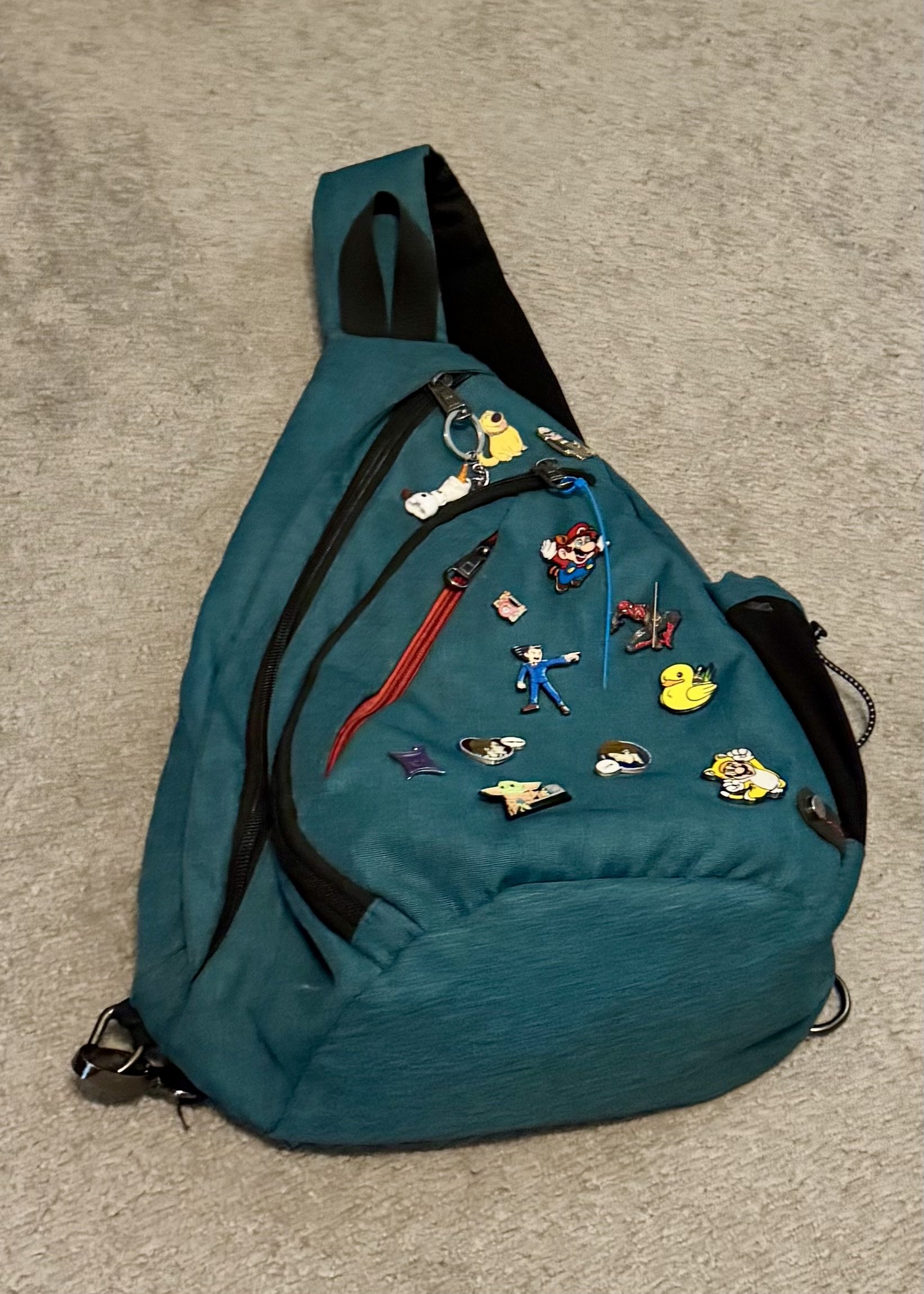 Teal crossbody sling backpack decorated with Nintendo character enamel pins